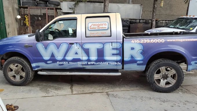 Blue and white plumbing service truck with 'WATERS' logo parked on street