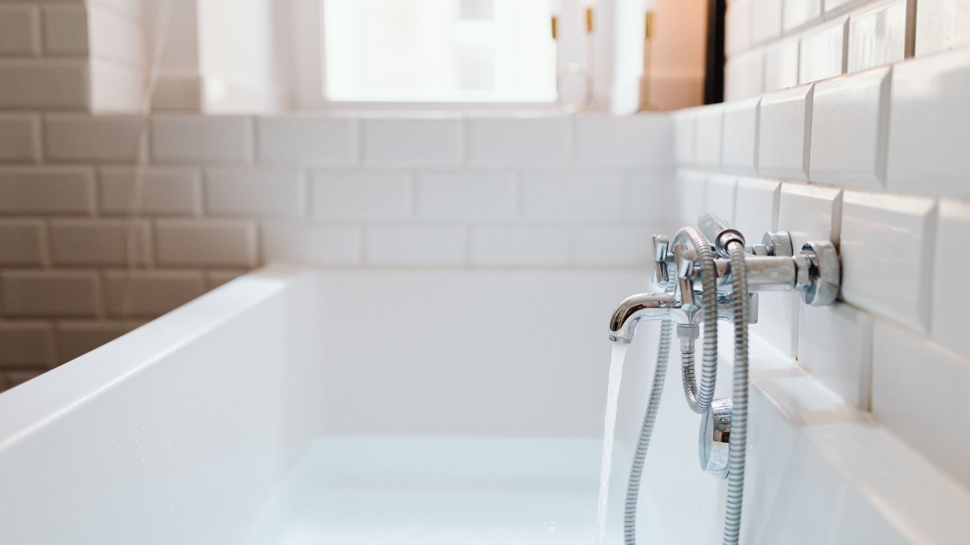 White bathtub with chrome faucet and handheld shower against tiled wall