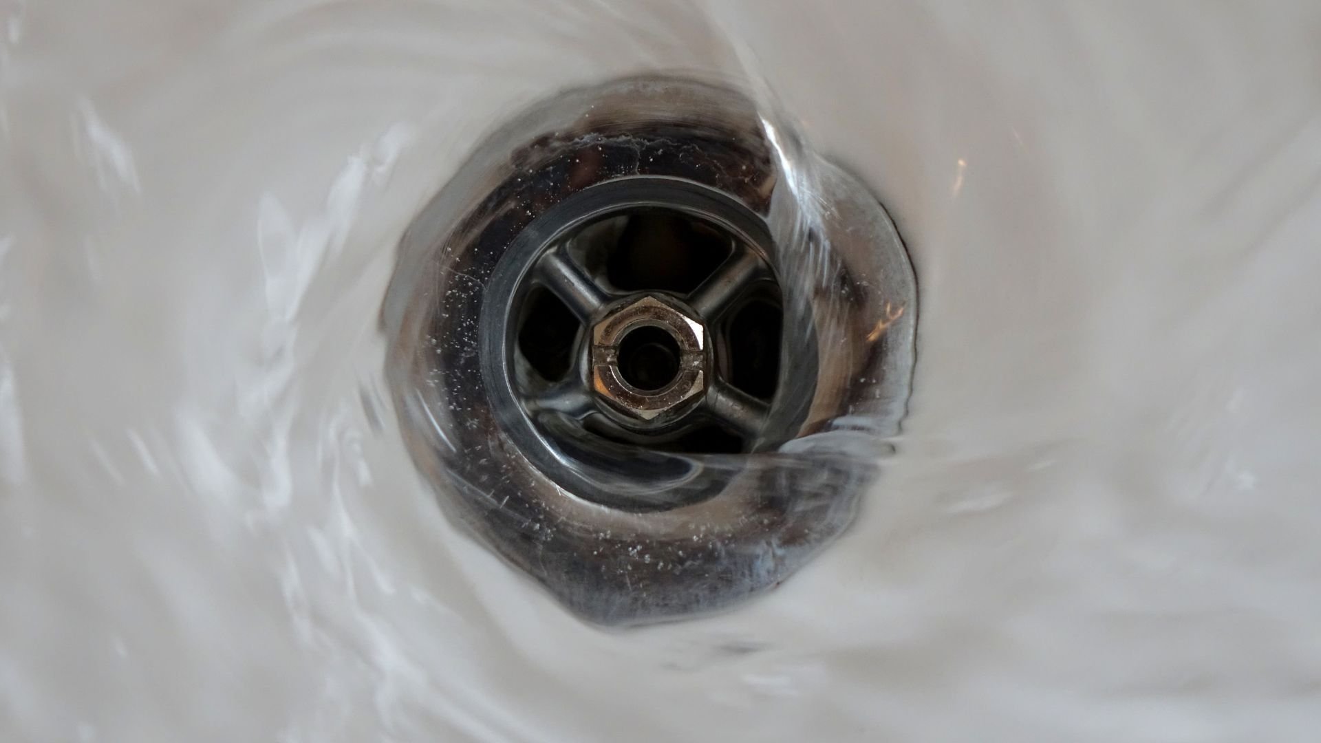 Close-up of a metallic drain with water swirling around its center