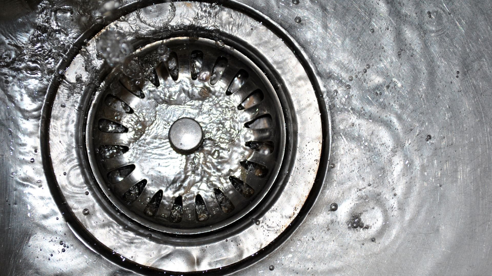 Close-up of a metal kitchen sink drain with water splashing around it