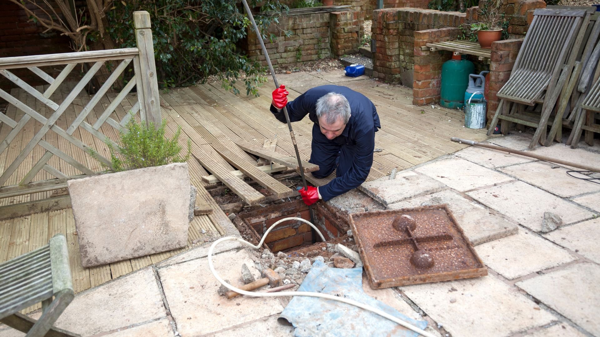 Person repairing drainage system in backyard with red gloves