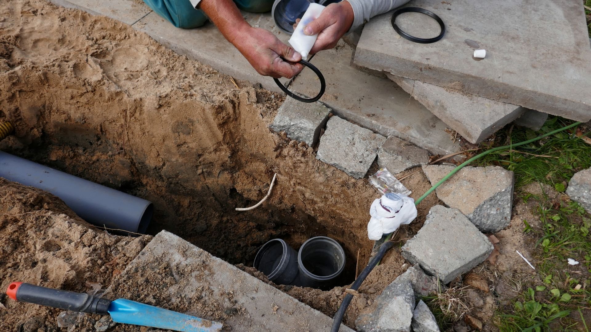 Worker installing drainage pipes in sandy ground with construction tools